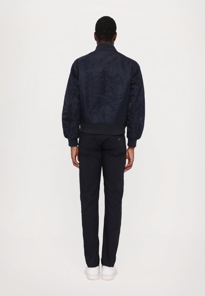 Navy bomber jacket with quilted texture, ribbed cuffs, and waistband, paired with slim-fit black pants and white sneakers.