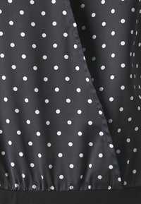 Blusa a pois caratterizzata da un tessuto nero con pois bianchi, dalla texture liscia e con orlo elastico nella parte inferiore, che crea una vestibilità rilassata.