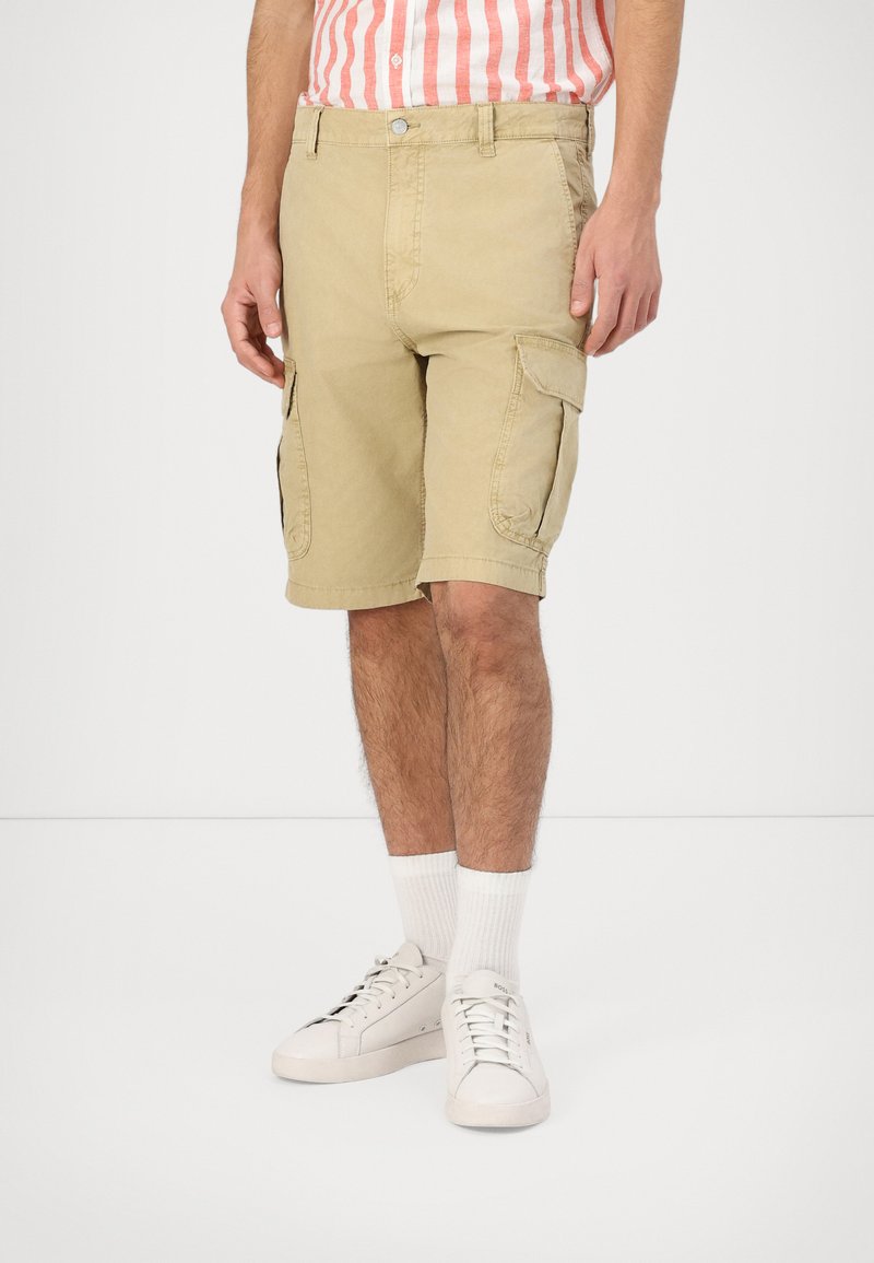 Shorts cargo color khaki realizzati in tessuto leggero, dotati di tasche laterali e una vestibilità comoda. Indossati con sneakers bianche e calze a coste.