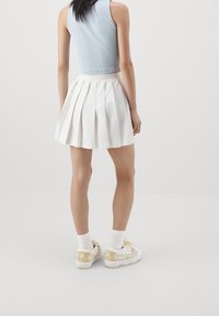 Witte geplooide rok met een hoge tailleband, gecombineerd met een lichtblauw cropped topje en witte sneakers met beige accenten. Gladde stoftextuur.