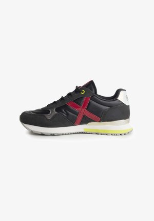 Černá a šedá sportovní bota s svrchním materiálem ze semiše a syntetiky, vybavená červeným designem ve tvaru X, žlutou okem a bílým s kovovým stříbrným akcentem na patě.