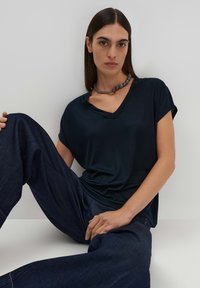 T-shirt a V scollo blu navy in tessuto morbido, maniche corte, abbinato a pantaloni a gamba larga in denim scuro. Presenta una collana con perline tonde.