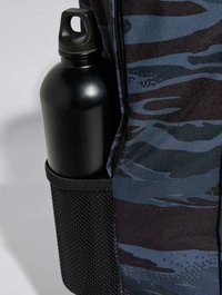 Botella de agua negra en un bolsillo lateral de malla de una mochila con patrón de camuflaje azul y gris, hecha de tela texturizada.