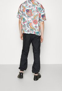 Lyhythihainen paita, jossa on värikäs kukkakuosi, yhdistettynä mustiin elastisiin housuihin ja mustiin kenkiin. Takakuva.