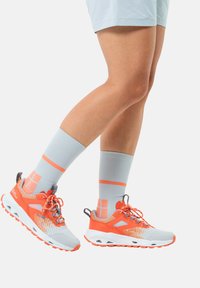 Grau-orangefarbene Sportschuhe mit strukturiertem Obermaterial, Netzpaneelen und Schnürsystem. Kombiniert mit hellblauen Socken, die orangefarbene Akzente haben.