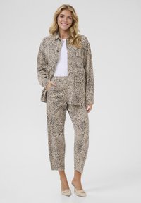 Veste en imprimé animal beige et pantalon assorti, avec une coupe décontractée et un tissu texturé. Un haut blanc et des talons de couleur claire complètent la tenue.