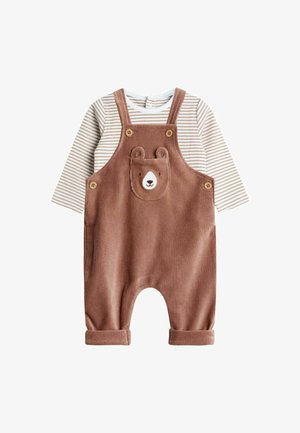 Pantalones de tirantes de pana marrón con un bolsillo con cara de oso, botones de madera y puños enrollados, combinados con una camisa de manga larga blanca a rayas.