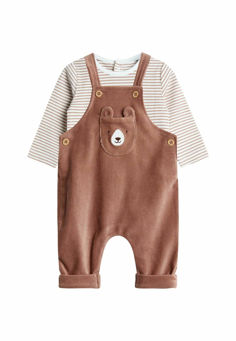Braune Corduroy-Latzhose mit Bärenkopf-Tasche, Holzknöpfen und aufgerollten Säumen, kombiniert mit einem weiß gestreiften Langarmshirt.