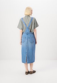 Denim overallkjole med rett snitt, lys blå farge, justerbare skulderstropper, to baklommer og splitt foran, kombinert med leoparden mønstrede leiligheter.