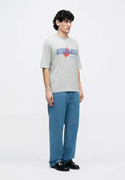 Graues T-Shirt mit kurzen Ärmeln und blau-rotem "DSQUARED2"-Logo, kombiniert mit locker sitzenden hellblauen Jeans und schwarzen Schuhen.