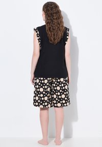 Zwart mouwloos topje met gerafelde randen, gecombineerd met zwarte shorts met grote beige stippen, gemaakt van zachte stof.