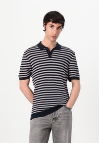 Stripet polo-skjorte i marineblå og lys grå, korte ærmer, med krave og knaplukning med tre knapper, parret med lys grå jeans.