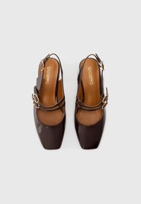 Brown patent leather slingback shoes with a square toe, two crossed straps, and a gold buckle detail on the side. Brown insoles.