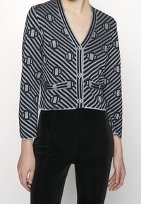 Cárdigan de punto en negro y azul con escote en V, patrón de rayas verticales, dos bolsillos delanteros y detalles en botones metálicos.