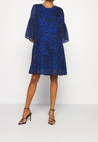 Blå leopardmönstrad klänning med genomskinliga, utsvängda ärmar. A-linjeformad silhuett med ett lagerat nederdel. Matchad med svarta sandaler med remmar.