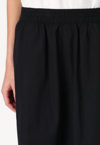 Jupe noire avec une taille élastique, présentant une texture lisse et une coupe fluide. Le tissu semble léger et résistant aux plis.