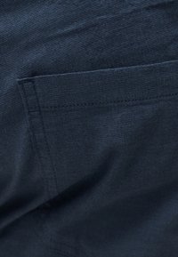 Κοντινή λήψη σκούρου μπλε υφάσματος που δείχνει λεπτομερή ραφή και υφή ορθογώνιας τσέπης.