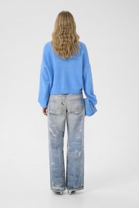 Sinine lühendatud kampsun lahtise lõikega, kombineeritud heledate kulunud laia lahusega teksadega. Juuksed lahtiste lainetena, vaade tagant.