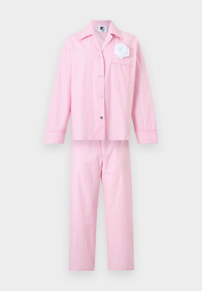 Ροζ και λευκή πιτζάμα με κατακόρυφες ρίγες, μακρυμάνικη πουκάμισο με κουμπιά και ταιριαστό παντελόνι, με ένα λευκό υφασμάτινο λουλούδι στην τσέπη του στήθους.