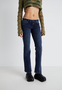 Mørkeblå jeans med rett ben-design, featuring en klassisk fem-lommestil og en sydd midje, kombinert med svarte tresko.