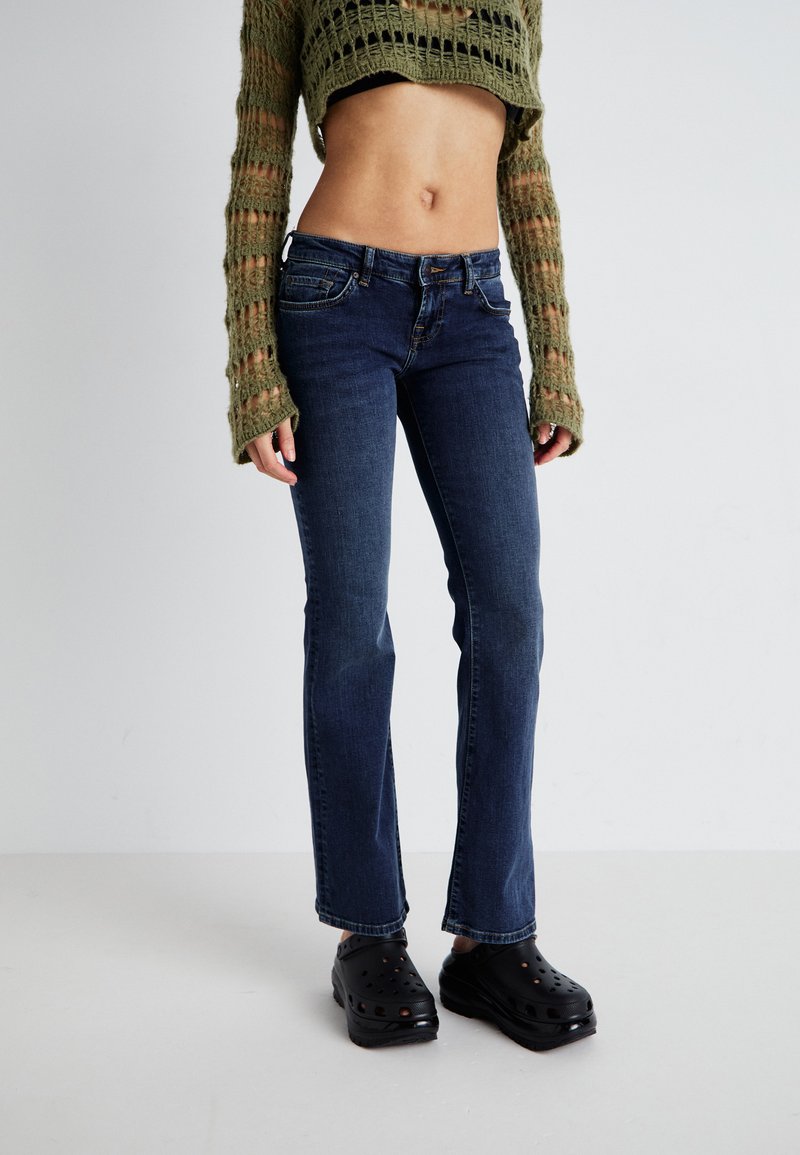 Mørkeblå jeans med rett ben-design, featuring en klassisk fem-lommestil og en sydd midje, kombinert med svarte tresko.