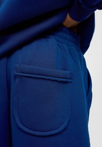 Blauwe joggers gemaakt van zachte stof met een elastische tailleband, voorzien van een rechthoekige zak op de dij met gestikte randen.