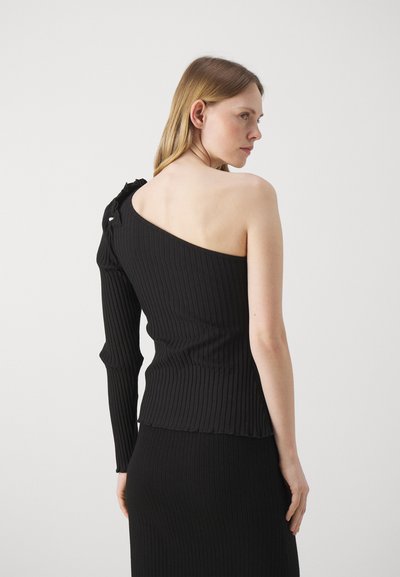 Asymmetrical black ribbed top with one long sleeve and one shoulder exposed, featuring a tie detail at the shoulder and fitted design.