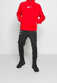 Röd Nike-huvtröja med en ficka fram och logotyp. Svarta Nike-sweatpants med logotypdetaljer. Svarta sneakers fulländar outfiten.