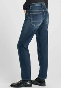 Jeans de mezclilla azul oscuro con un diseño de pierna recta, que presentan costuras visibles, bolsillos traseros y detalles desgastados cerca del dobladillo.