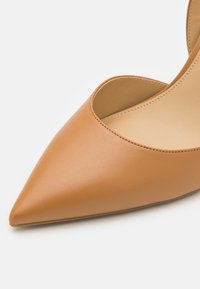 Scarpa a punta in pelle color cuoio con design a ritaglio e texture liscia. Presenta uno stile minimalista e una finitura opaca sottile.