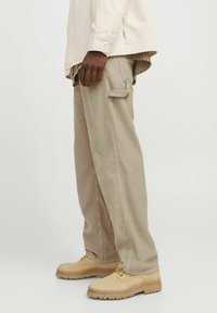 Beige flanelle broeken met een losse pasvorm, voorzien van zijzakken en uitlopende manchetten, gecombineerd met lichtbruine veterschoenen.