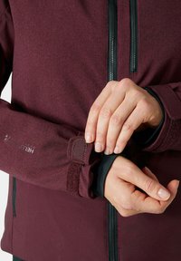 Giacca bordeaux con zip nere, polsini regolabili e chiusura in velcro. Tessuto morbido e design aderente adatto per attività all'aperto.
