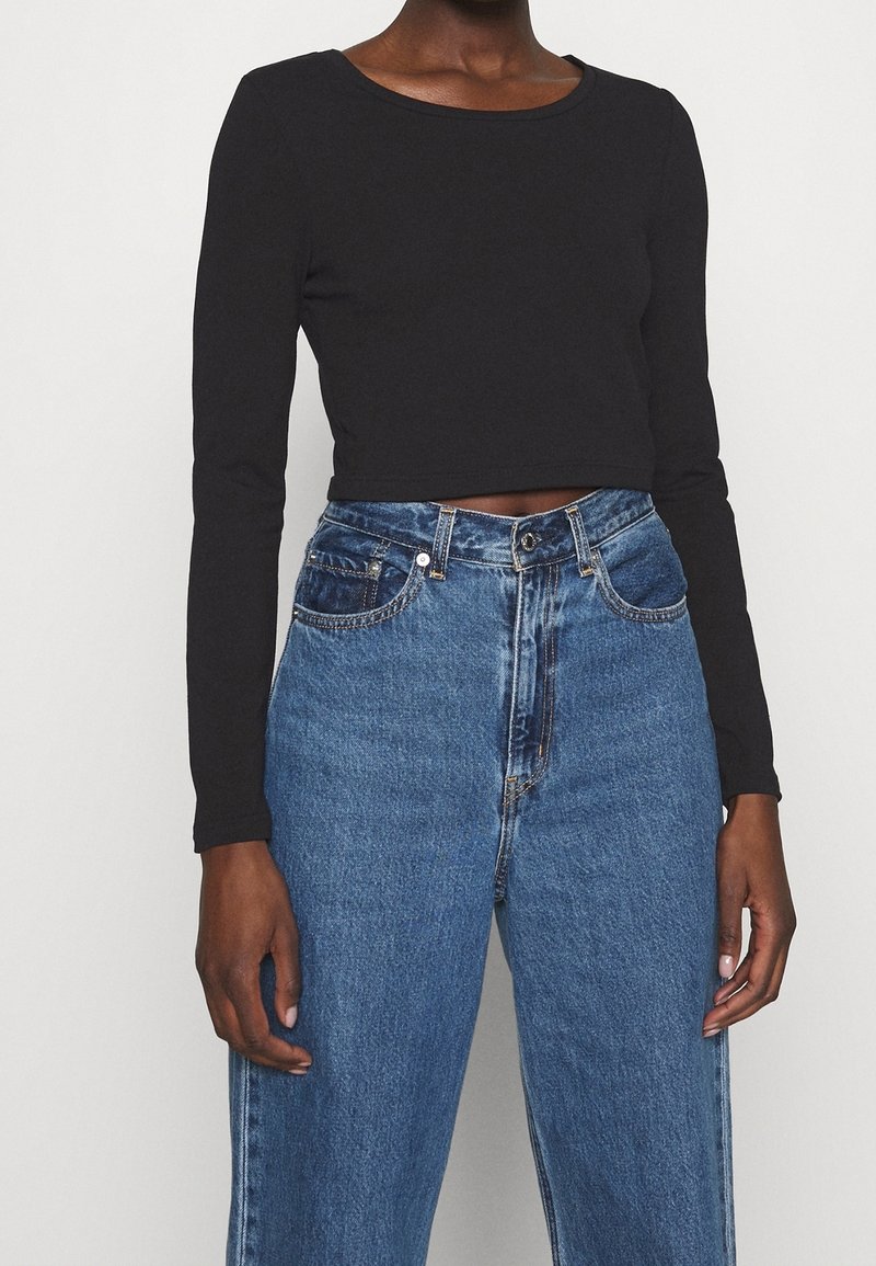 Svart långärmad crop top som matchas med högmidjade blå denimjeans. Toppen har en rund halsringning och en figurnära design.