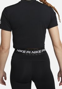 Černý sportovní top s krátkými rukávy, doplněný černými legínami s bílým páskem s logem značky. Hladká látka s přiléhavým střihem.