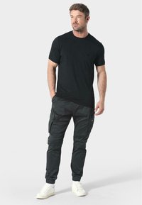 Czarny t-shirt z krótkim rękawem i okrągłym dekoltem, w połączeniu z ciemnymi spodniami cargo z kieszeniami po bokach i ściągaczami na kostkach, noszony z białymi sneakersami.