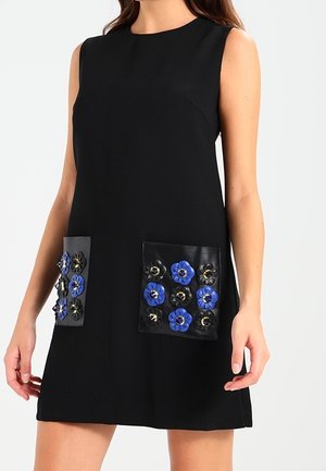 Ærmeløs sort kjole med to forlommer dekoreret med blå og sorte blomsterapplikationer.