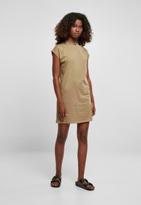Khaki bawełniana sukienka t-shirtowa z krótkimi, zwiniętymi rękawami, prostym krojem, okrągłym dekoltem i minimalistycznym designem. Noszona z czarnymi sandałami na płaskiej podeszwie.