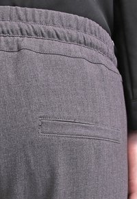 Pantalones grises de tela tejida con cintura elástica y un bolsillo trasero con apertura horizontal. Textura suave, diseño ajustado.