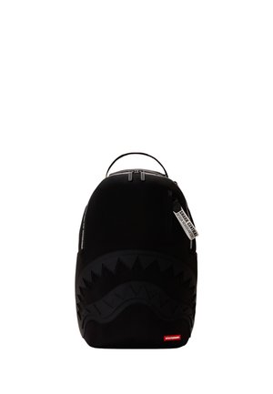 Zaino nero con grafica di denti di squalo sul davanti, doppia cerniera superiore e etichetta bianca con la scritta "SHARK CENTRAL Design Headquarters."