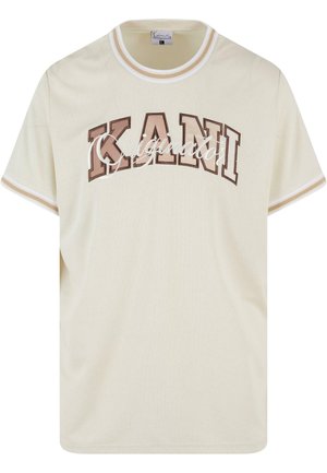 Krém színű póló, texturált felülettel, barna blokk betűkkel "KANI" és "Original" írással. Fehér csíkokkal díszítve.