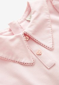 Tissu rose doux avec col à bord festonné et deux petits boutons en forme de cœur sur un vêtement pour enfants.