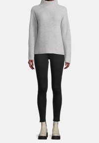 Grå randig tröja med hög krage, kombinerad med svarta tajta byxor och beige ankelstövlar. Lätt textur, gedigen design och figurnära silhuett.