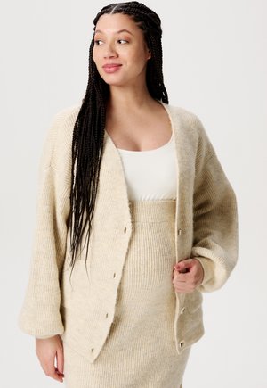 Beige melierter Cardigan mit lockerer Passform, weiten Ärmeln und Knopfverschlüssen, getragen über einem passenden gerippten Tanktop und Rock.