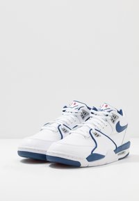 Witte Nike sneakers met blauwe accenten, voorzien van een gladleren bovenwerk, ronde veters, zichtbare luchtkussens en mesh gedeelten voor ademend vermogen.