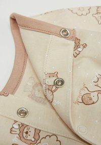 Béžová bavlněná tkanina má zvířecí vzory v hnědé barvě. Výstřih má kontrastní terakotový lem s kovovými drukovými zapínáními.