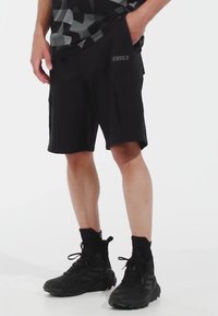 Svarta cargo-shorts med lös passform, som har sidofickor och en diskret logo. I kombination med svarta hög-top skor och ankelsockor.