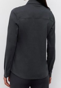 Camicia button-up grigia scura con maniche lunghe, caratterizzata da un colletto classico e una cucitura sulla parte posteriore. Vestibilità slim, realizzata in tessuto morbido con polsini abbottonati.