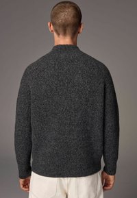 Grauer gestrickter Pullover mit strukturiertem Finish, ausgestattet mit einem hohen Kragen und leicht fallenden Schultern. Der Saum ist gewölbt.