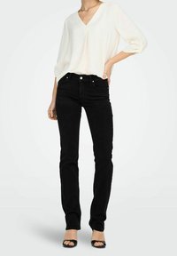 Jeans de mezclilla negra combinados con una blusa crema de escote en V. La blusa tiene mangas de tres cuartos y los jeans presentan un diseño ajustado.