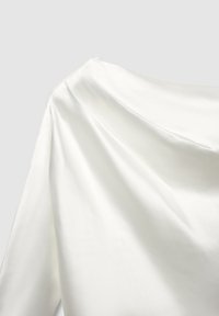 Weißer Satin-Stoff, der mit einer glatten Textur fällt und ein plissiertes Design mit einem leicht offenen Ausschnitt aufweist, was die Schlichtheit betont.